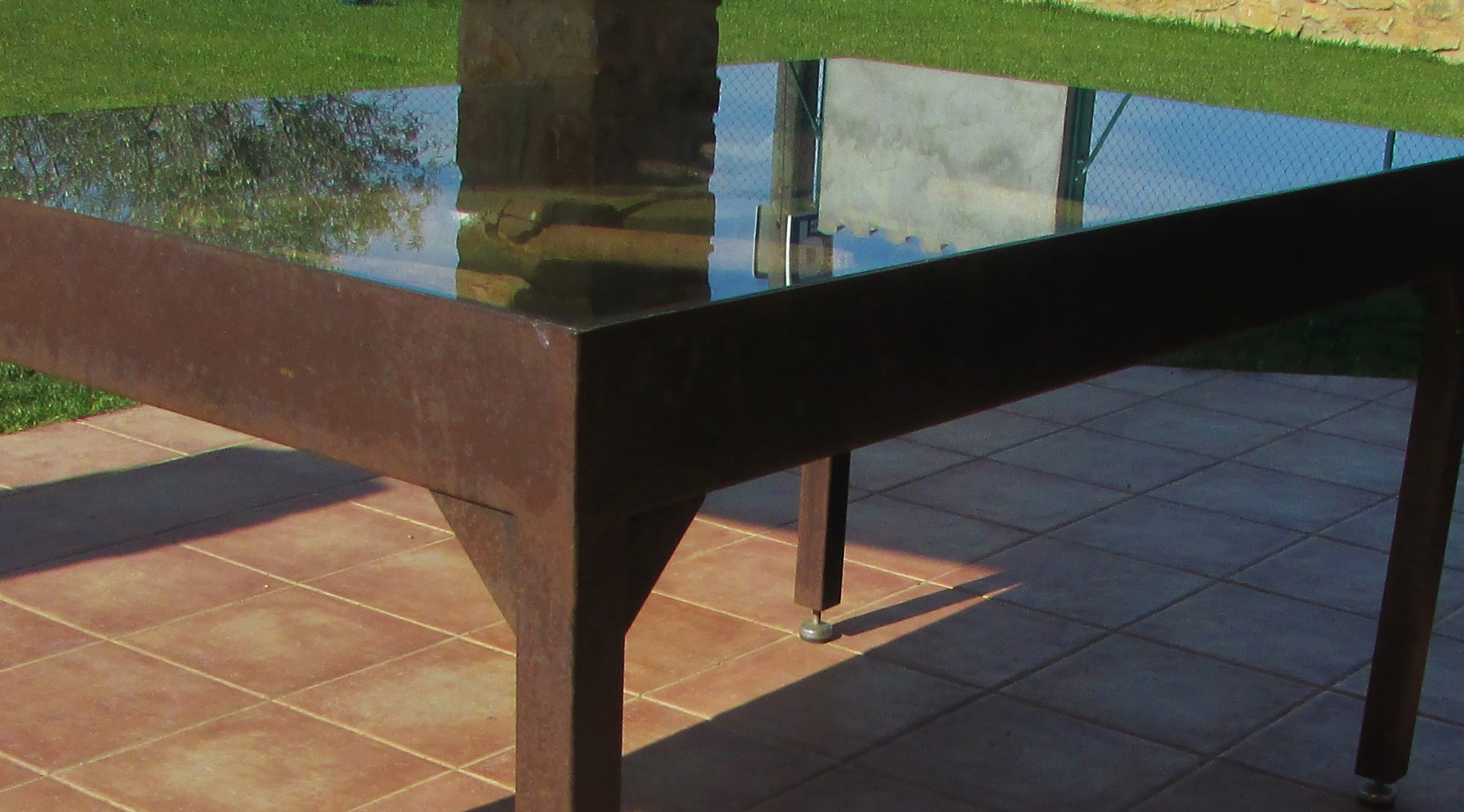 Mesa de exterior elegante en estructura de forja con superficie de vidrio