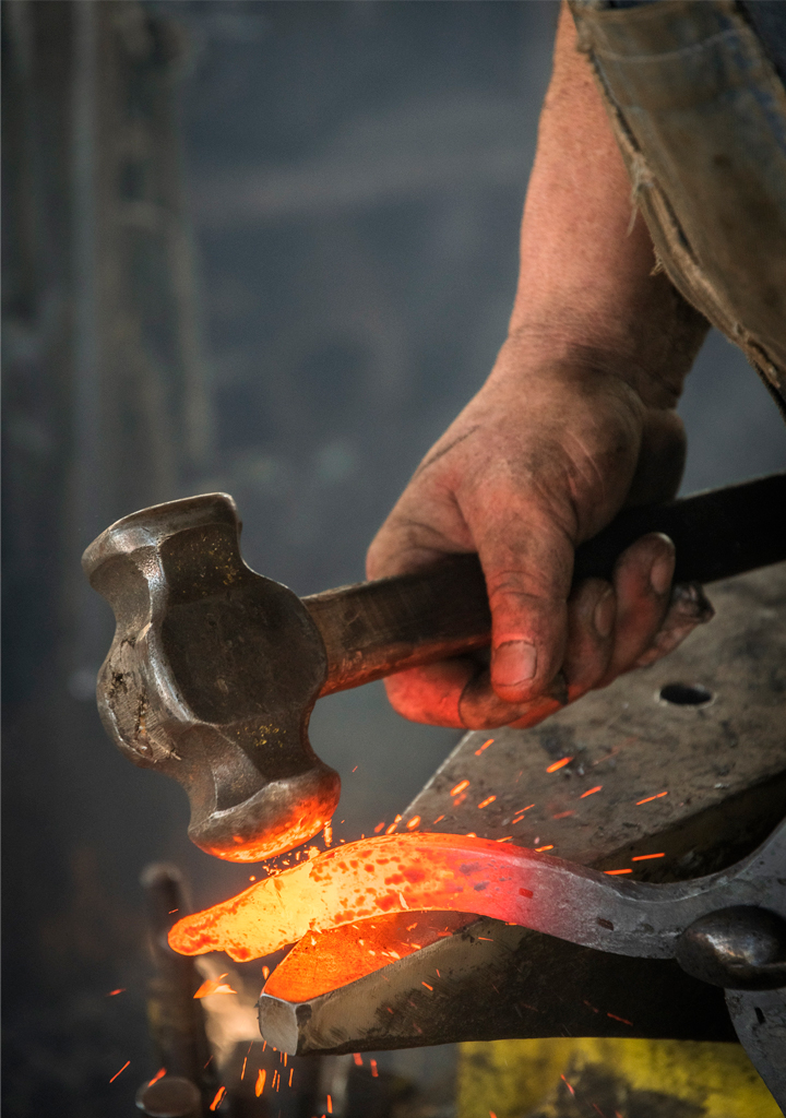 Obrero experto trabajando en un yunque en taller de herrería